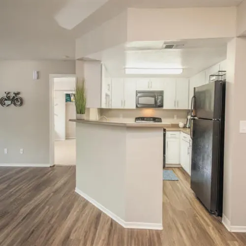 Open apartment kitchen with breakfast bar, white cabinets, black refrigerator, and wood-look flooring