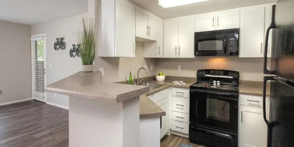 Apartment kitchen with white cabinets, breakfast bar, black stove and refrigerator, and wood-look flooring