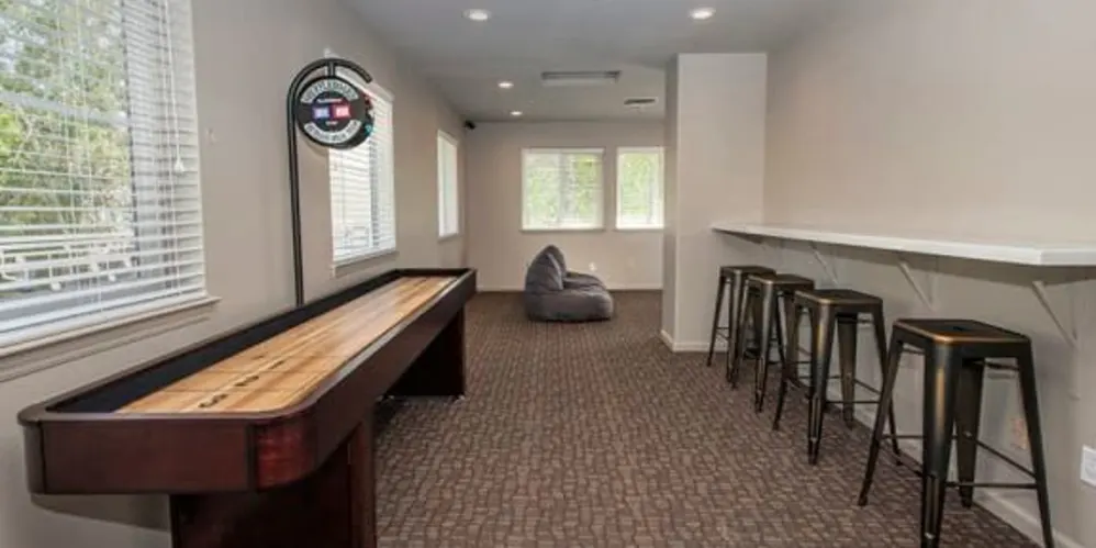 Community game room with shuffleboard table, bar counter with stools, and bean bag seating