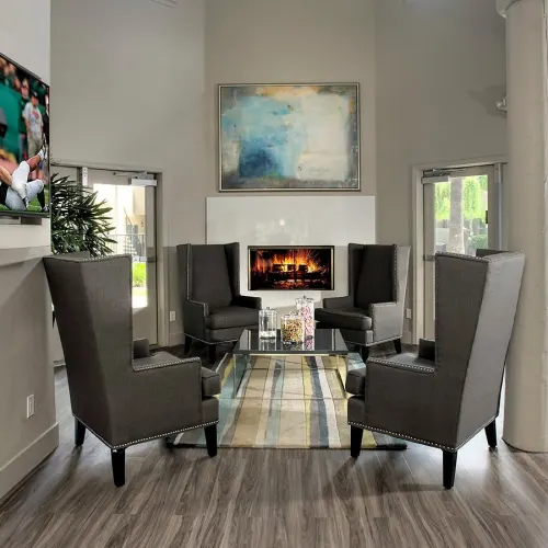 Apartment community lounge with fireplace, four armchairs, coffee table, and wall art