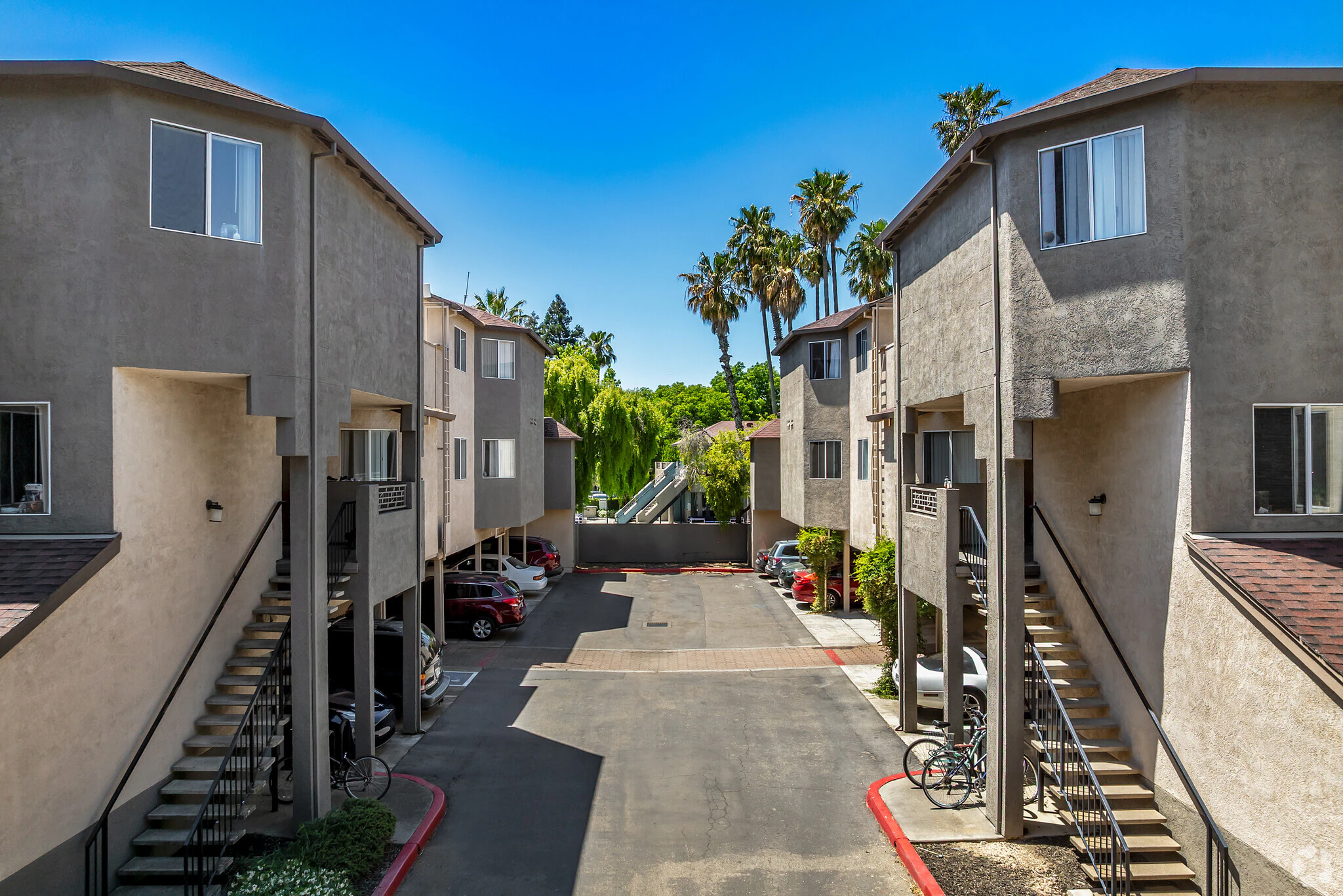 Courtyard between two-story stucco student apartment buildings with parking and palm trees