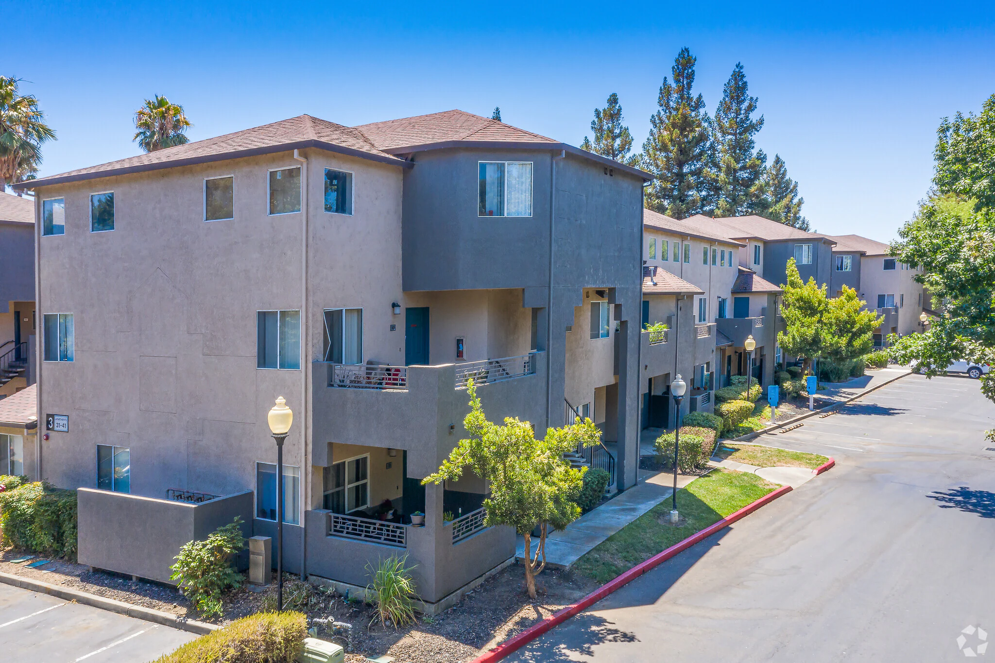 Exterior view of Sharps Flats student apartments with balconies, trees, and parking lot near UC Davis
